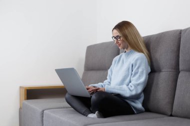 Female programmer typing code on laptop at home. Young woman coding on notebook computer while sitting on couch 