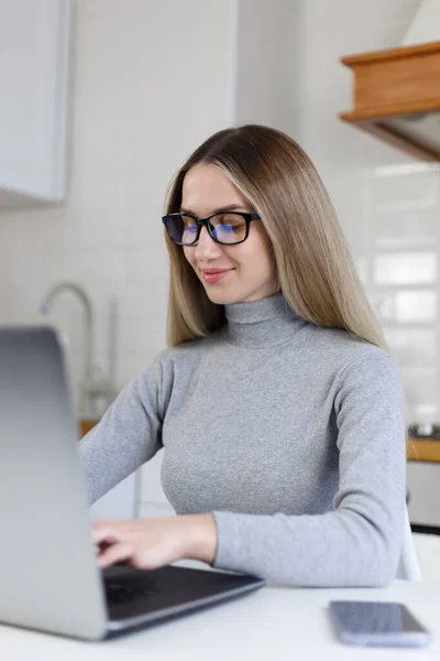 Freelance writer woman typing text on laptop computer in home kitchen. Natural looking white female works on modern notebook pc