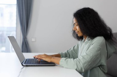 Focused BIPOC woman typing text on notebook keyboard. Programmer coding on laptop computer at home