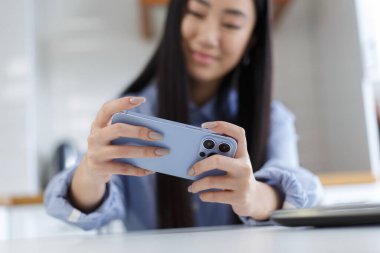 Asian girl plays mobile game on smart phone. Close up photo of cheerful Vietnames female person enjoys playing online games on modern gadget