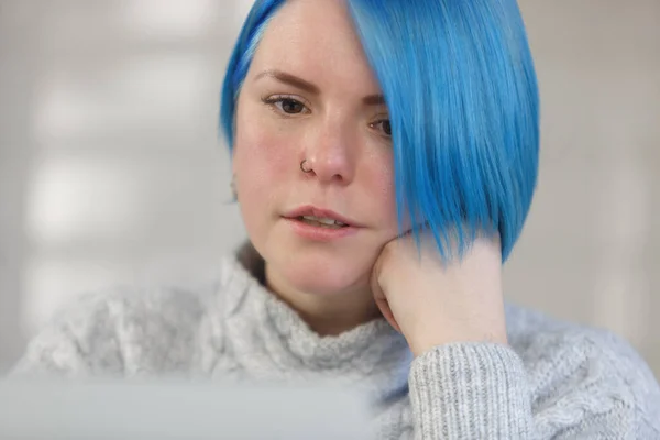 Close up portrait of millennial woman with bob haircut and dyed blue hair. Focused female person reading text from computer screen