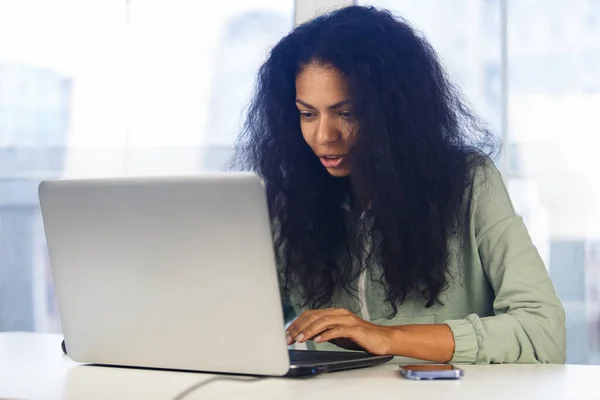Young black woman works on laptop at home. Freelancer BIPOC female doing distant work online