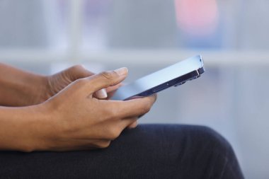 Hands of black female person typing a message on smart phone. Young adult POC woman using modern mobile phone with big touch screen