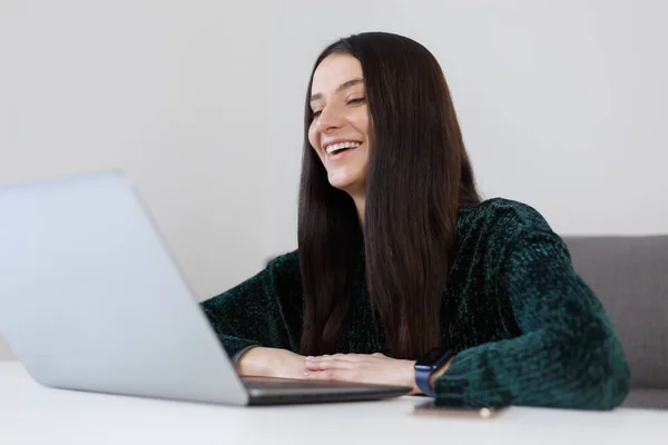 Happy young woman talking on web camera and laughing. Cheerful white female person speaking on video call at home