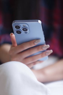 Young girl using modern smart phone. Close up photo of young adult woman browsing mobile app on blue phone with triple camera
