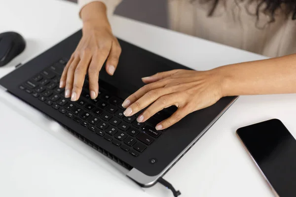 Young black woman typing text on laptop keyboard. POC female working on modern notebook pc in overhead photo