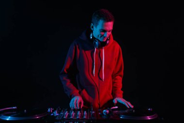 Cheerful young DJ scratching vinyl record on party in night club. Cool white disc jockey person playing music set on stage with a smile