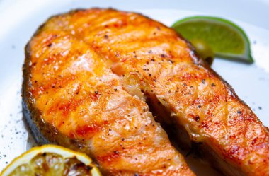 Salmon fish steak cooked on grill in seafood restaurant and sered on white plate with lemons