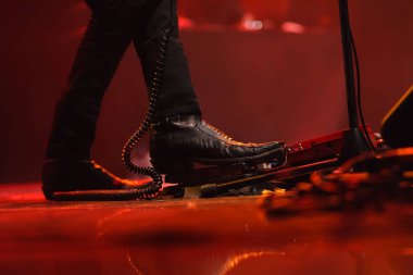 Cool rock singer in stylish leather boots playing on electric guitar. Musician using pedal effector for bass guitar on concert