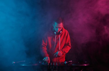 Disc jockey mixing hip hop music with vinyl records and sound mixer in smoke on stage. Night club DJ plays set with turntables