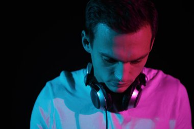 Young DJ playing music. Portrait of white man wearing professional headphones in neon lights