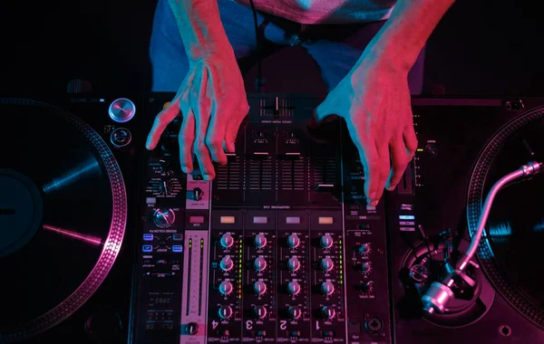 DJ plays music with turntables and sound mixer, shot on stage from above. Professional disc jockey playing set in night club
