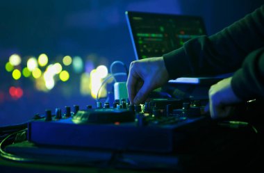 DJ gece kulübünde elektronik müzik seti çalıyor. Disk jokeyinin müzik parçalarını midi denetleyici aygıtıyla karıştırdığı fotoğrafı kapat