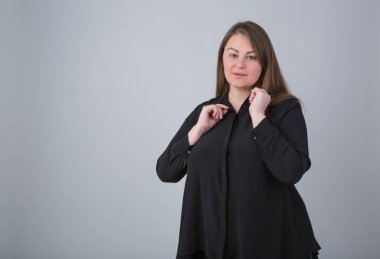 Good looking overweight woman in black casual shirt posing in studio. Cheerful plus size female model