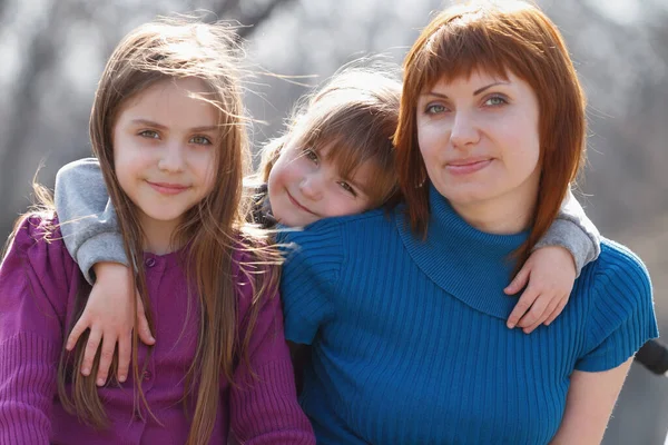 Happy family portrait. Ukrainian mother and two little sisters posing outdoor in sunny spring day. Friendly and natural looking Ukrainians in Europe