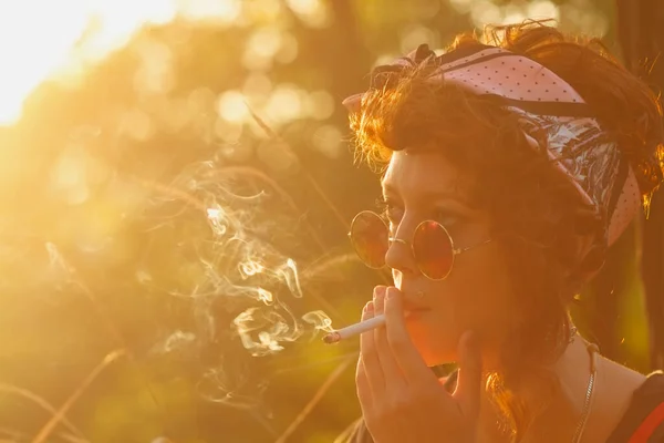 清凉的年轻嬉皮士女孩在日落时在户外抽烟 带雪茄嘴的时尚乌克兰模特的肖像 — 图库照片