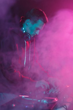 Gece kulübü DJ 'i kalın duman ve parlak sahne ışıkları altında müzik çalıyor. Beyaz adam konserde disk jokeyi rolünde oynuyor.