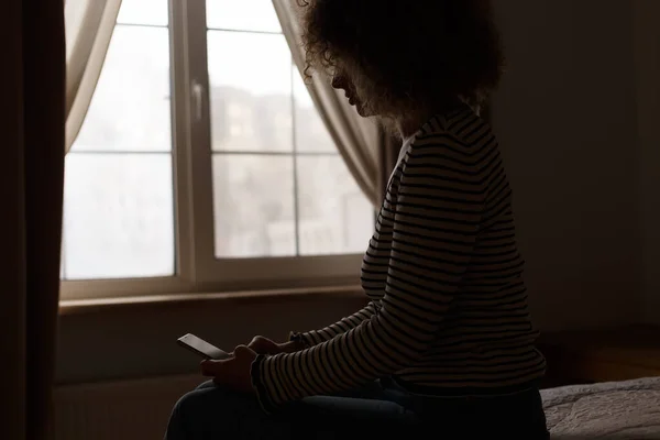 Силуэт Молодой Женщины Сидящей Кровати Темной Спальне Печатающей Сообщение Смартфоне — стоковое фото