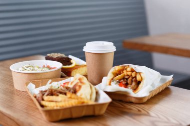 Greek fast food dinner served in recyclable dishware on table. Souvlaki, gyros, fries and salad in disposable plates clipart