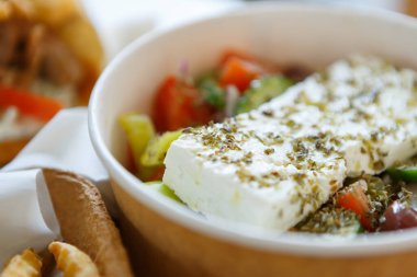 Geleneksel Yunan salatası, peynirli, zeytinyağlı ve yumuşak sebzeli kağıt tabakta servis edilir.