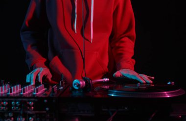 Kırmızı kapüşonlu havalı genç DJ gece kulübünde pikaplara plak çiziyor. Hip hop DJ 'inin elleri sahnede müzik çalıyor.