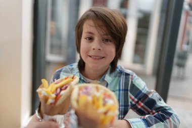 Yunan fast food restoranında küçük mutlu bir çocuğun portresi. Tatlı beyaz çocuk ızgara tavuk eti ve patates kızartmasıyla jiroskop yiyecek.