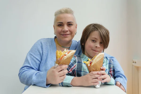 Happy family eating Greek gyros. Portrait of cheerful white woman with short hair and her little son enjoying fast food in a cafe