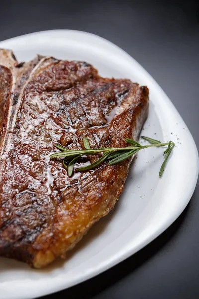 グリルで調理されたTボーンステーキには レストランのホワイトプレートにローズマリーハーブが添えられています 肉料理店で夕食のために用意されたおいしいアメリカの牛肉 — ストック写真