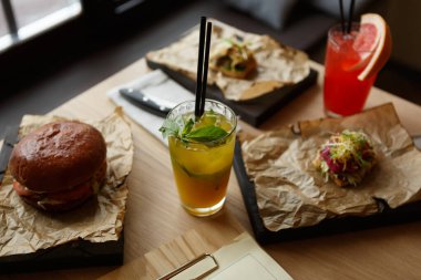 Mojito kokteyli, hamburgerler ve mezeler restoranda dekoratif parchement kağıtları ve ahşap tabaklar üzerinde servis ediliyor. Bir kafede uzun içkilerin ve gurmenin tadını çıkar.