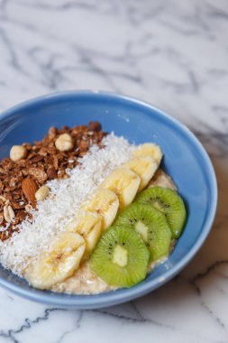 Mermer masada servis edilen sağlıklı kahvaltı yemeğiyle bir kase. Beyaz pirinç, dilimlenmiş kivi ve öğle yemeği için hazırlanmış fındıklı muzlar.