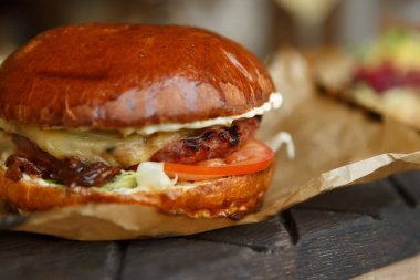 Restoranda ahşap bir tahtanın üzerinde servis edilen büyük bir çizburger. Erimiş peynirli ve taze sebzeli nefis Amerikan hamburgeri.