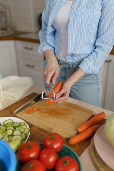 House wife prepares lunch with fresh vegetables. Woman peeling carrots with a peeler tool. Female person cooking healthy vegetarian meal at home