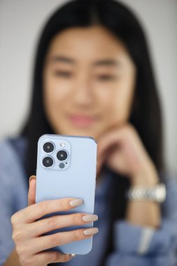 Asyalı kız akıllı telefondan arıyor. Güzel Vietnamlı kadın modern mavi cep telefonunun ön kamerasında konuşuyor.