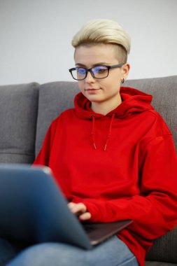 Genç programcı kadın evdeki kanepede otururken dizüstü bilgisayarda kod yazıyormuş. Gözlüklü beyaz inek modern defter bilgisayarı üzerinde çalışıyor.