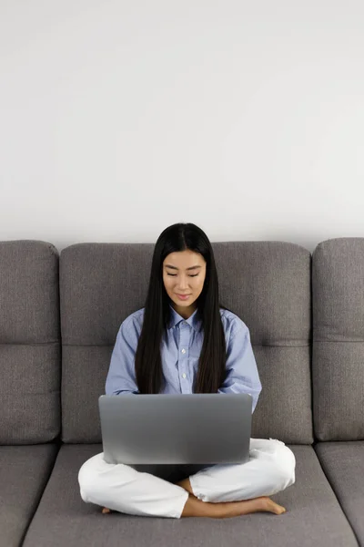 Asian girl coding on laptop computer. Vietnamese female studying on modern notebook while sitting on couch at home