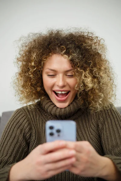 Excited young woman with smartphone. Portrait of happy white female reading a message on social media app in mobile phone