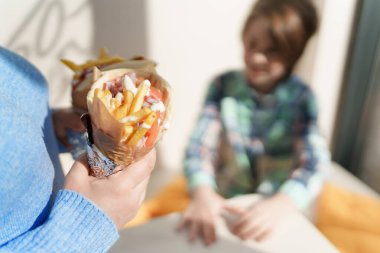 Kadın öğle yemeğinde küçük bir çocuğa jiroskoplu sandviç veriyor. Anne ve oğul bir kafede geleneksel Yunan fast food 'unun tadını çıkarıyorlar