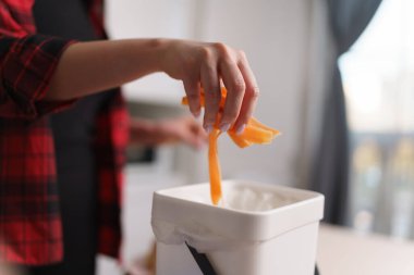 Sebzeleri geri dönüşüm kutusunda soyan bir kadın. Ev hanımı yemek pişiriyor ve organik atıkları evdeki Bokashi konteynırında pişiriyor.