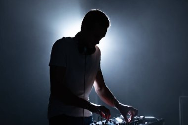 Gece kulübündeki bir DJ 'in silueti. Havalı genç adam sahnede müzik çalıyor.