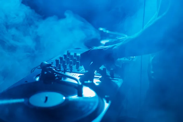 Silhouette of a club DJ mixing music in smoke on stage. Professional disc jokey plays set on techno party