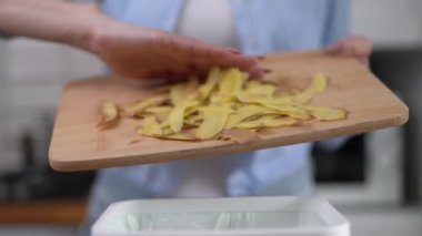 Kadın gübre kutusuna organik gıda atıkları atıyor. Kadın aşçı, evdeki bir markette patates kabuklarını geri dönüştürüyor.