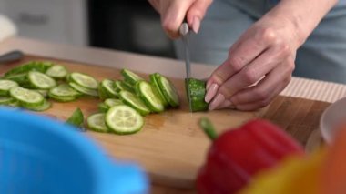 Mutfak masasında bıçakla salatalık kesen kadın elleri. Sağlıklı vejetaryen yemeği pişiren ve gübre kabuklarını bir bokashi kutusunda soyan bir kadın.