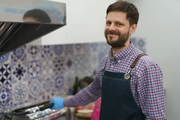 在商业厨房用围裙烹调食物的友善白人的画像 快乐的白人男性在电炉中做饭 — 图库照片