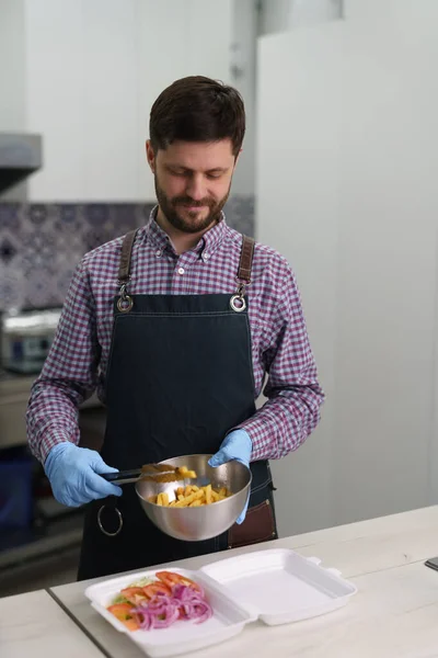 一个快乐的白人男人在商业厨房里准备传统的希腊快餐 厨师用薯条和蔬菜准备卡拉马基菜 — 图库照片