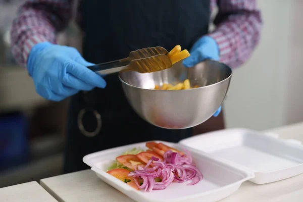 在餐馆里煮午饭盒 厨师在餐馆里烹调传统的希腊卡拉马基菜 厨师把薯条放在一个装有红葱片和西红柿的容器里 — 图库照片