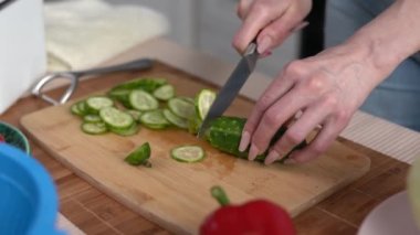 Kadın evcil bir mutfakta ahşap bir tahtanın üzerinde salatalık kesiyor. Bayan öğle yemeği için taze salata hazırlıyor.