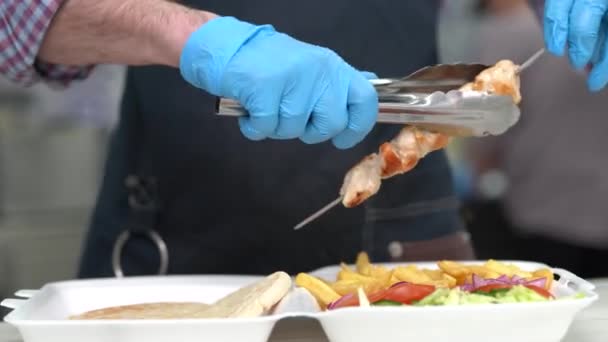 厨师把烤好的肉放进一个装有传统希腊卡拉马基菜的午餐盒里 厨师用钳子吃猪肉片 — 图库视频影像