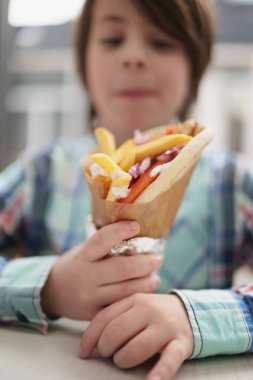 Pide ekmeğine sarılı jiroskoplu sandviç tutan aç küçük çocuk. Beyaz çocuk ızgara et, patates kızartması ve tzatziki soslu geleneksel Yunan fast food 'unun tadını çıkarıyor