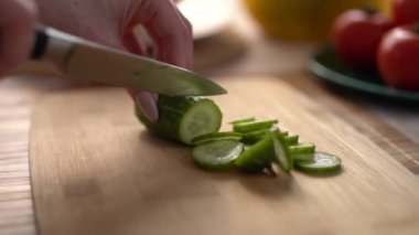 Bıçaklı bir kadın, tahta bir tahtada taze salatalık kesiyor. Kadın evde öğle yemeği için sağlıklı yeşil salata hazırlıyor.