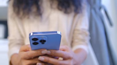 Genç siyahi kadın mavi telefondan üçlü kameralı bir mesaj yazıyor. Tanımlanamayan POC 'lu kadın cep telefonuyla internette mesajlaşıyor